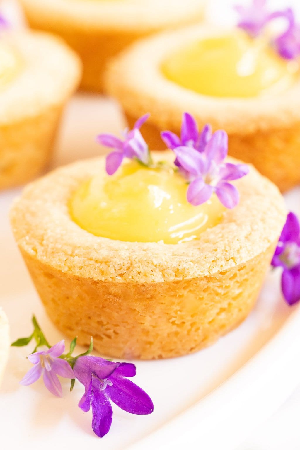 Vertical extreme closeup photo of a batch of Lemon Curd Shortbread Tarts decorated with blue edible flowers.