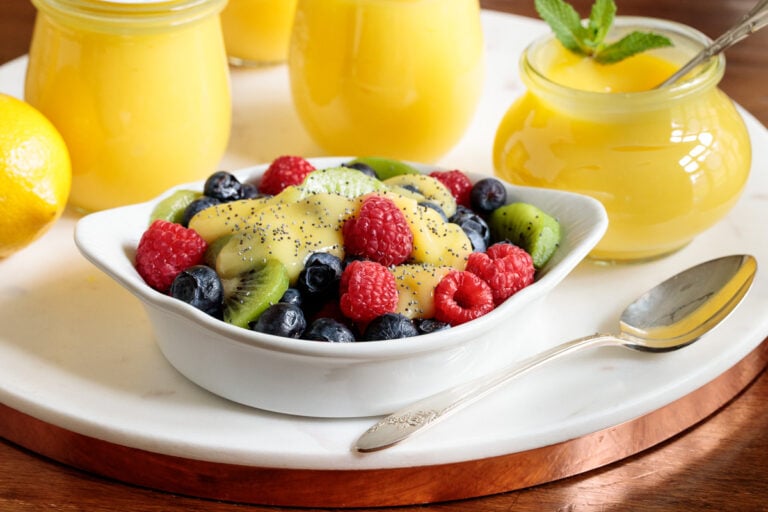 Horizontal closeup of a bowl of fresh fruit surrounded by jars of Ridiculously Easy Microwave Lemon Curd.