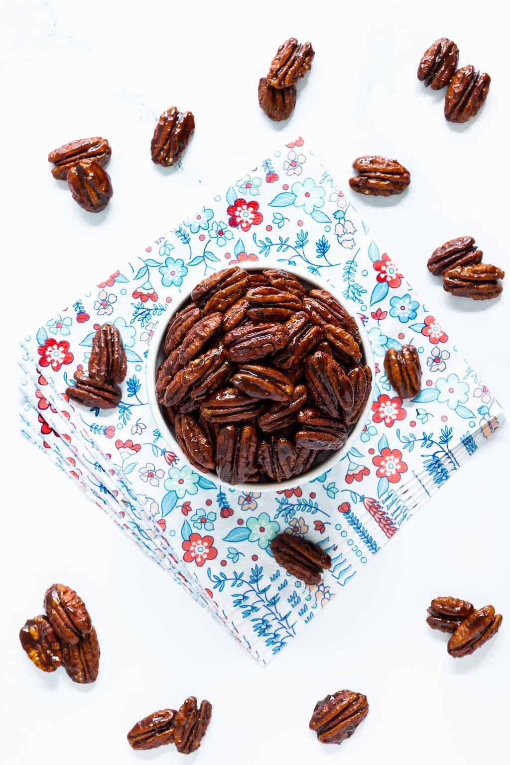 Vertical overhead photo of a batch of Southwest Sweet and Spicy Glazed Pecans in a light blue ramekin on a decorative napkin.