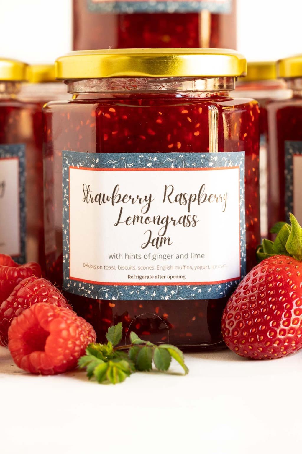 Vertical ultra closeup photo of jars of Strawberry Raspberry Lemongrass Jam featuring custom gift labels for the jars.