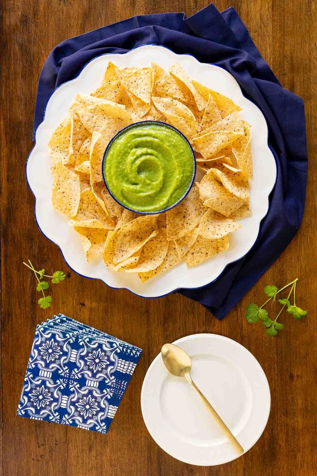 Vertical overhead photo of a dish of Fresh Tomatillo Avocado Salsa surrounded by a plate of tortilla chips.