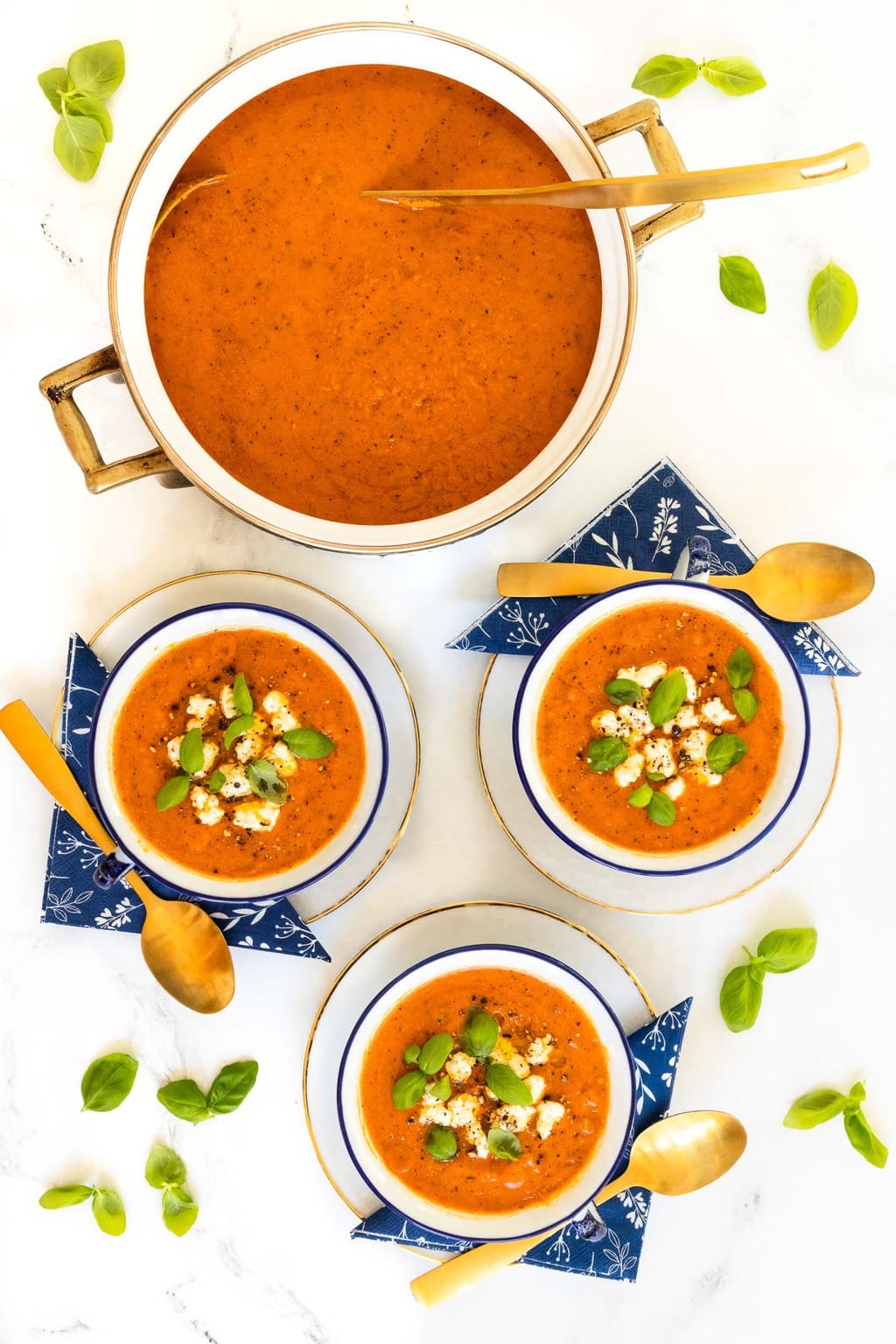 Vertical overhead photo of bowls and a pot of Tomato Basil White Bean Soup surrounded by and garnished with fresh basil leaves.