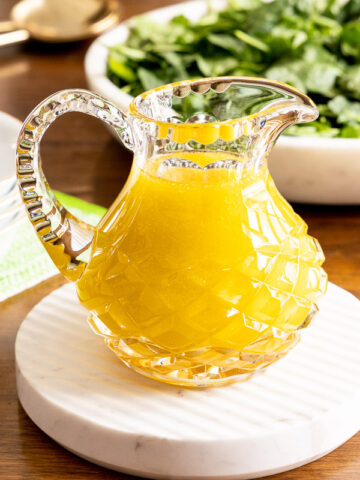 Horizontal photo of a cut glass pitcher filled with Honey White Balsamic Dressing on a wood table.