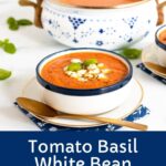 Vertical photo of a bowl and pot of White Bean Tomato Basil Soup surrounded by fresh basil leaves with a large word title graphic at the bottom of the photo.