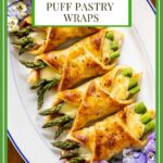 Vertical overhead photo of a serving plate filled with Asparagus Prosciutto Puff Pastry Wraps decorated with edible pansy flowers.