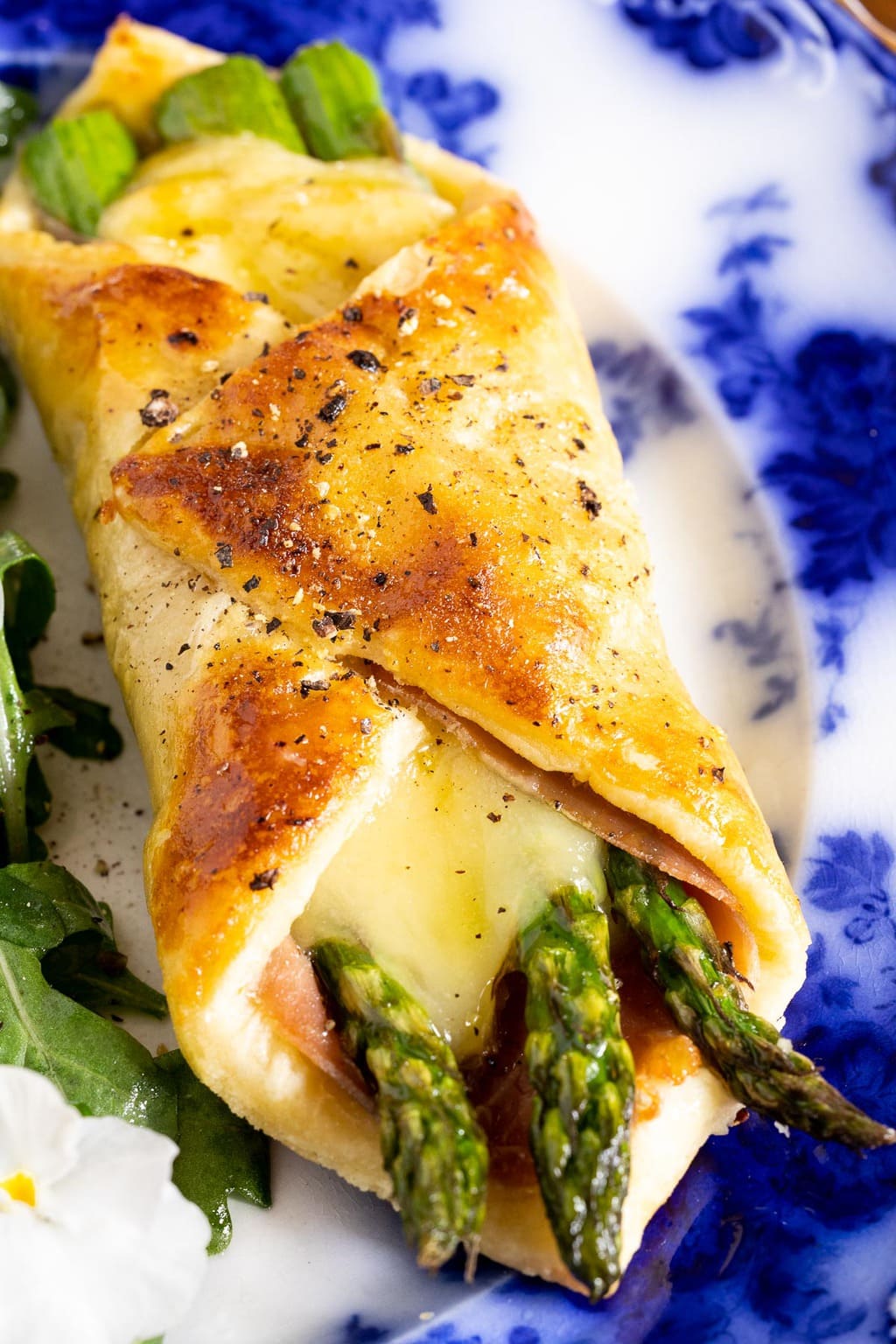 Vertical closeup photo of a Honey-Glazed Asparagus Prosciutto Puff Pastry Wrap on a Flo blue serving plate.