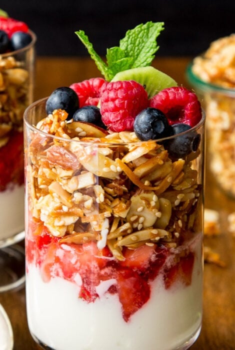 Horizontal closeup photo of several Double Almond Coconut Granola Parfaits garnished with fresh fruit and mint leaves.