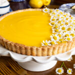 Horizontal closeup photo of a French Lemon Tart decorated with edible chamomile flowers.