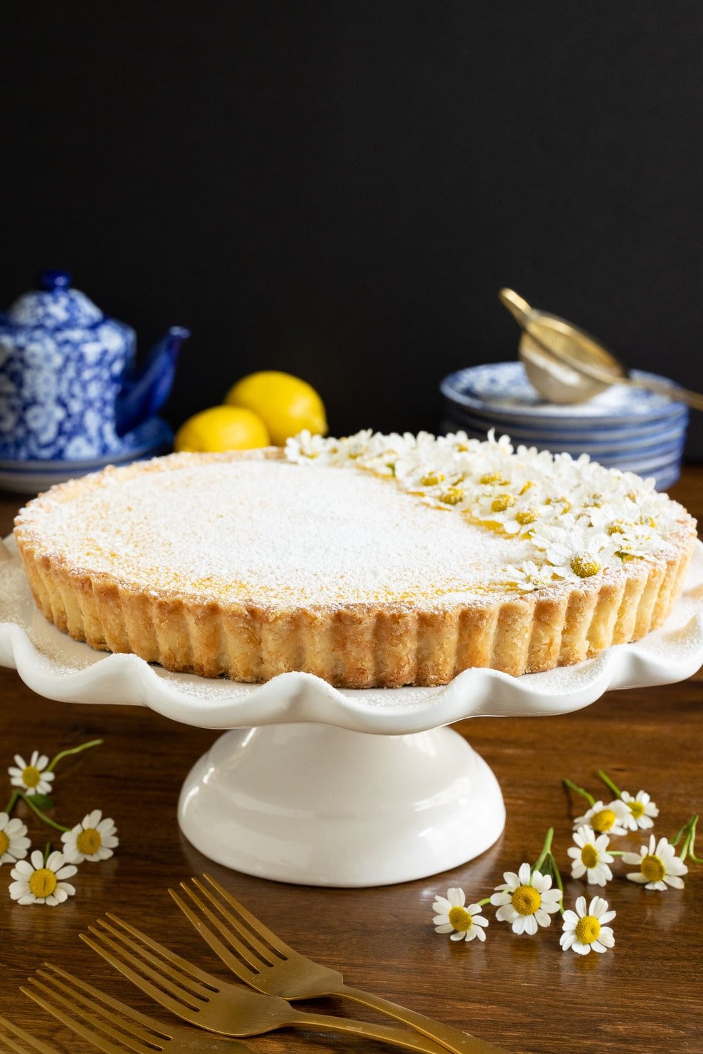 Vertical photo of a French Lemon Tart sprinkled with powdered sugar and decorated with edible camomile flowers.