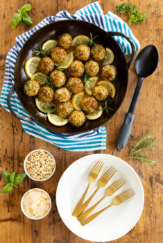 Vertical overhead photo of Herbed Chicken Meatballs in a cast iron skillet with gold forks and white plates.