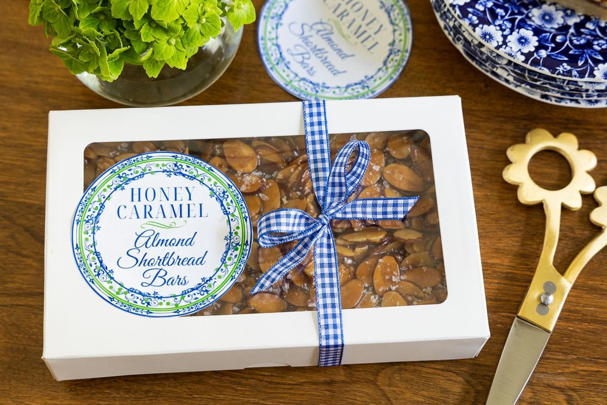 Horizontal overhead photo of a gift box filled with Honey Caramel Almond Shortbread Bars a custom printed label for gift giving.