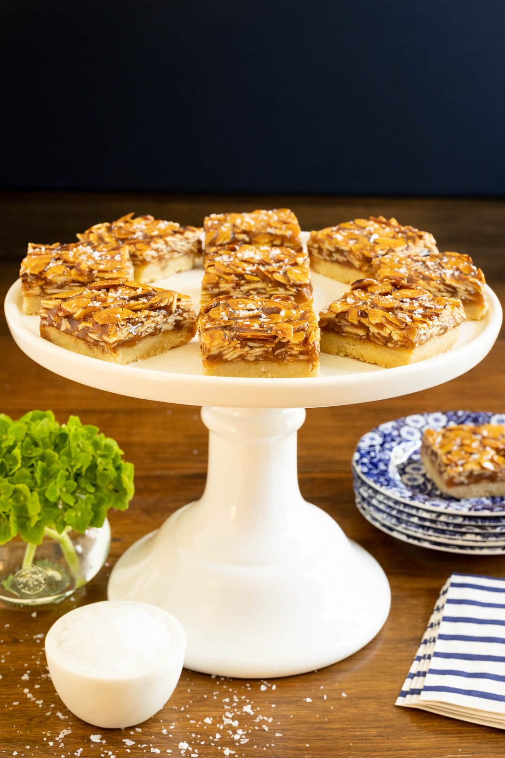 Vertical photo of a batch of Honey Caramel Almond Shortbread Bars on a white pedestal serving plate.
