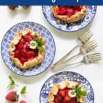 Vertical overhead photo of three Fresh Strawberry Galettes on blue and white patterned plates garnished with fresh mint leaves and flowers.
