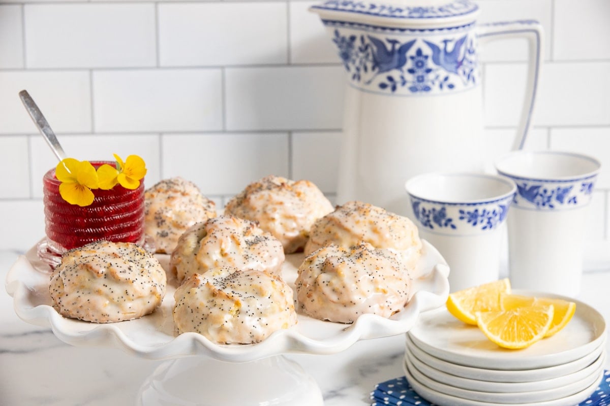 Horizontal photo of a batch of Ridiculously Easy Lemon Poppy Seed Scones on a white scalloped pedestal serving plate.