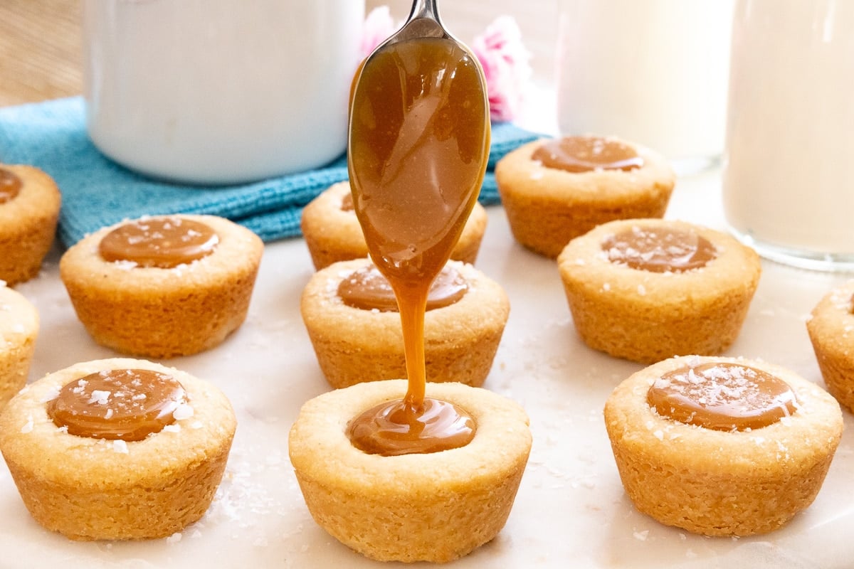 Horizontal closeup photo of spooning caramel into the wells of Ridiculously Easy Salted Caramel Shortbread Bites.