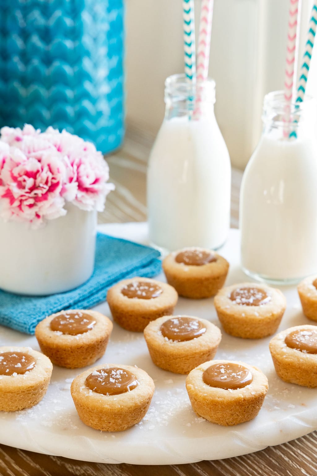 Vertical picture of Salted Caramel Shortbread Bites with jars of milk and pink flowers