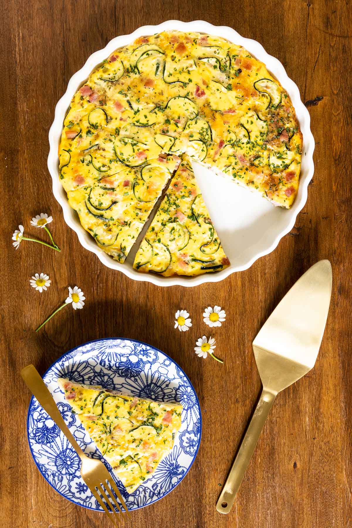 Vertical overhead photo of Southwestern Zucchini Ham Crustless Quiche with a slice cut on a blue and white serving plate.