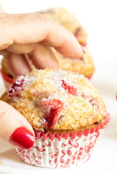 Horizontal closeup of a hand taking a Fresh Strawberry Buttermilk Muffin.