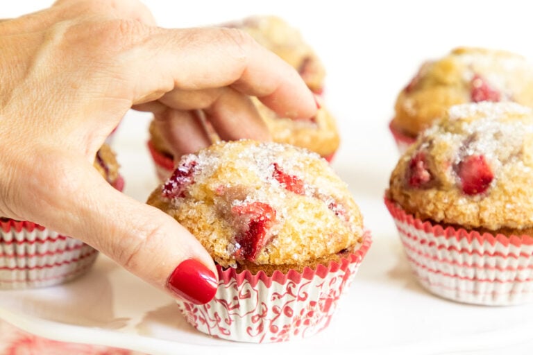Horizontal closeup of a hand taking a Fresh Strawberry Buttermilk Muffin.