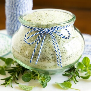 Horizontal photo of a glass Weck jar filled with Tuscan Herbed Sea Salt (Sale alle Erbe) and surrounded by fresh herbs.