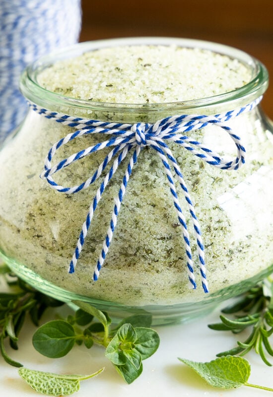 Horizontal photo of a glass Weck jar filled with Tuscan Herbed Sea Salt (Sale alle Erbe) and surrounded by fresh herbs.