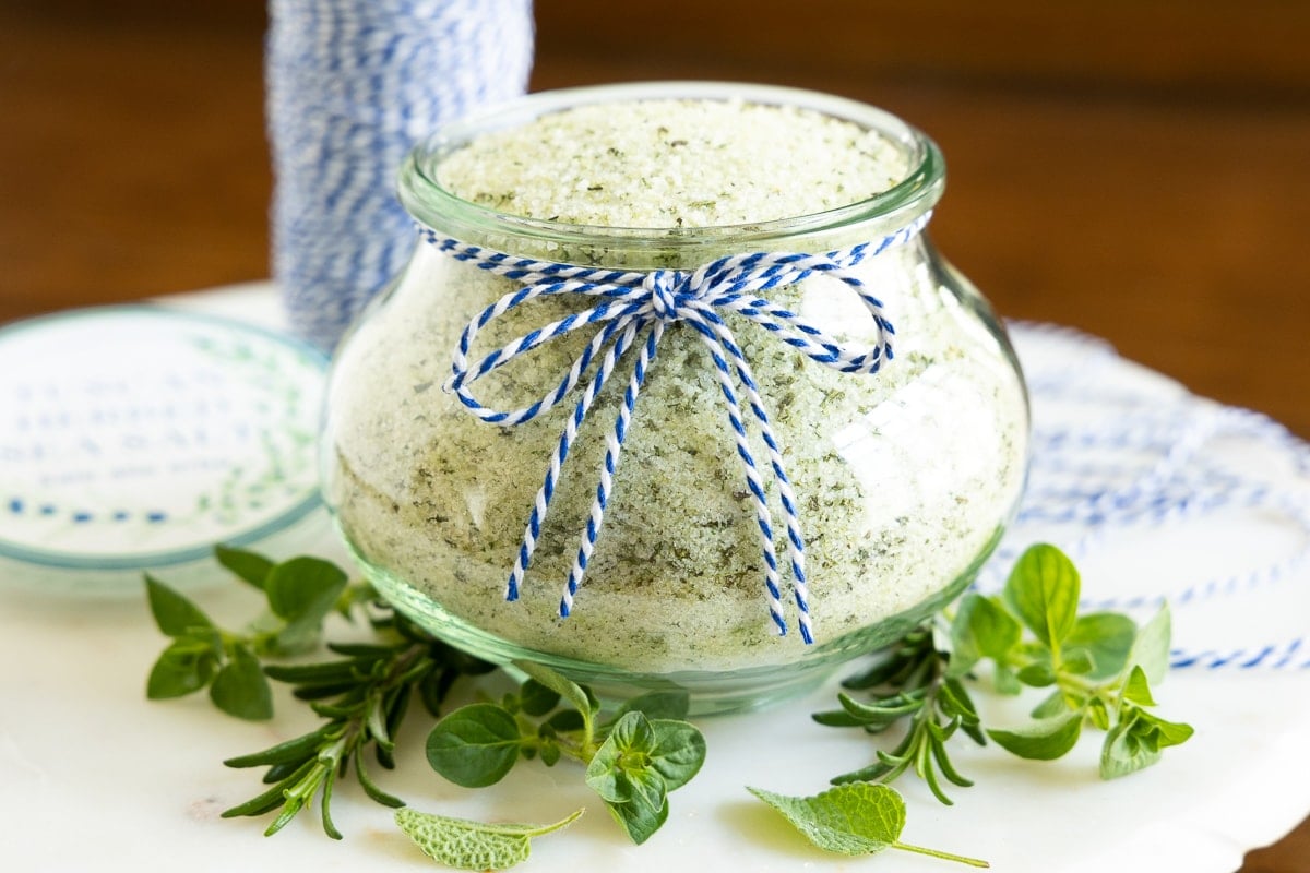 Horizontal photo of a glass Weck jar filled with Tuscan Herbed Sea Salt (Sale alle Erbe) and surrounded by fresh herbs.
