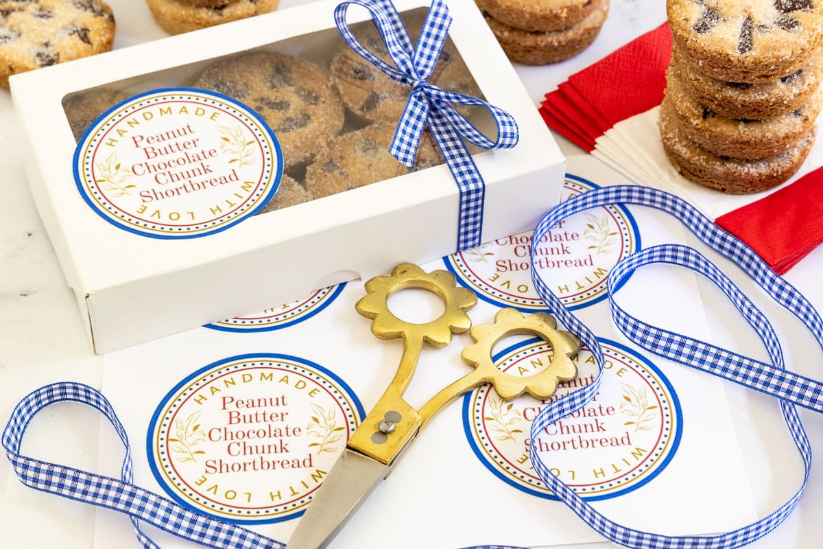 Horizontal photo of a batch of Ridiculously Easy Peanut Butter Shortbread Cookies packaged in gift boxes decorated with blue and white checked ribbon and custom gift labels.