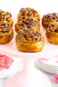Horizontal photo of a batch of Ridiculously Easy Sticky Pecan Rolls on a pale pink pedestal plate.