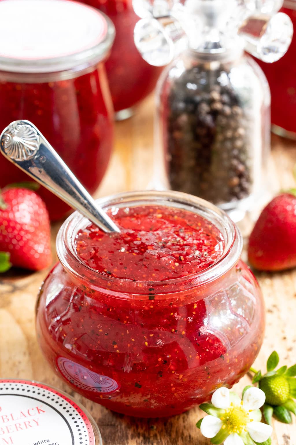 Vertical closeup photo of Strawberry Balsamic Black Pepper Jam in a Weck jar with a spoon dipped in.