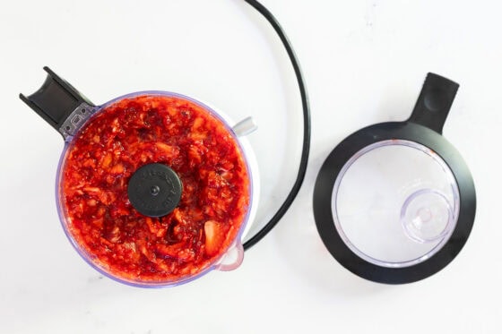 Overhead view of chopped strawberries in a food processor bowl, prepared for making homemade strawberry freezer jam.