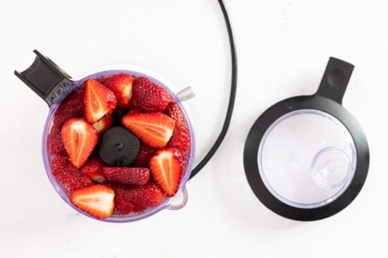 Overhead view of fresh strawberries in a food processor bowl, prepared for making homemade strawberry freezer jam.