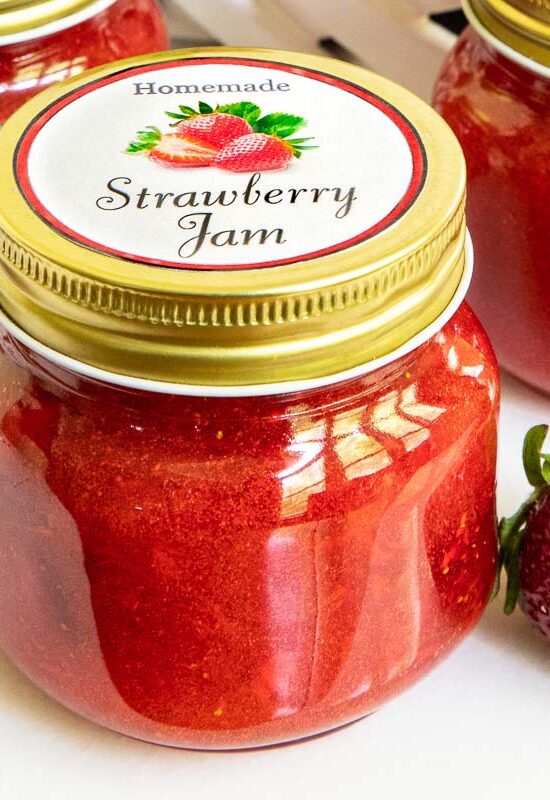 Horizontal closeup photo of a batch of Strawberry Jam in jars with custom labels for gift giving.