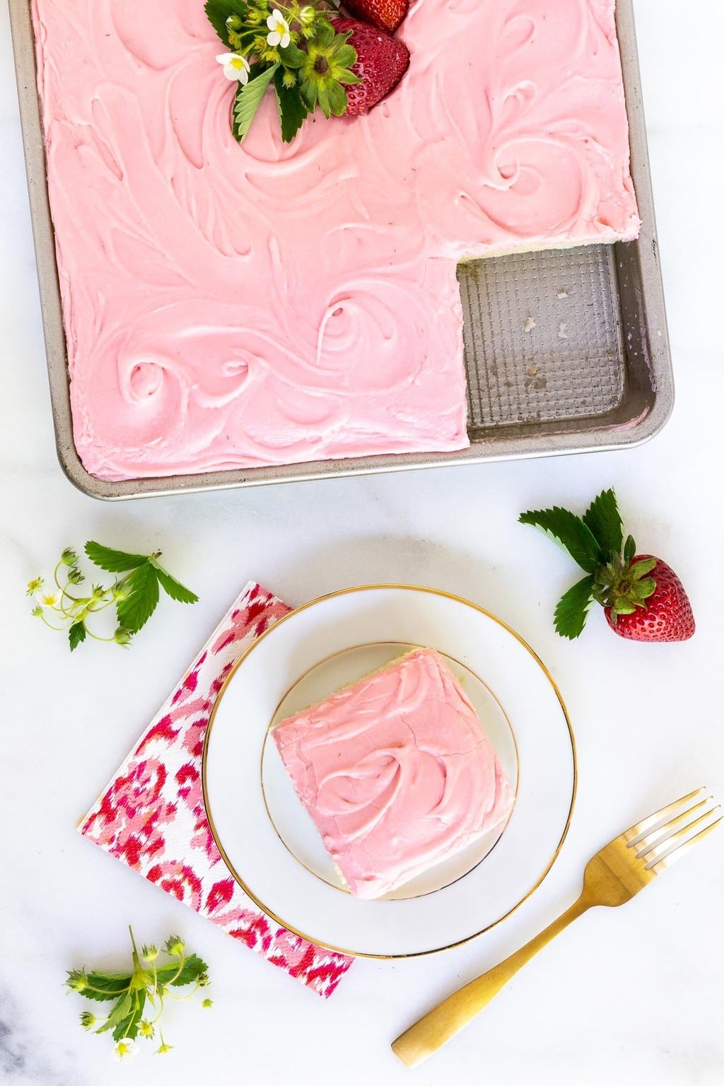 Vertical overhead photo of a Vanilla Bean Sheet Cake with Fresh Strawberry Icing with a slice cut out on a serving plate.