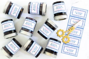 multiple jars of blueberry jam complete with custom labels laid out on a white surface with a pair of decorative gold scissors