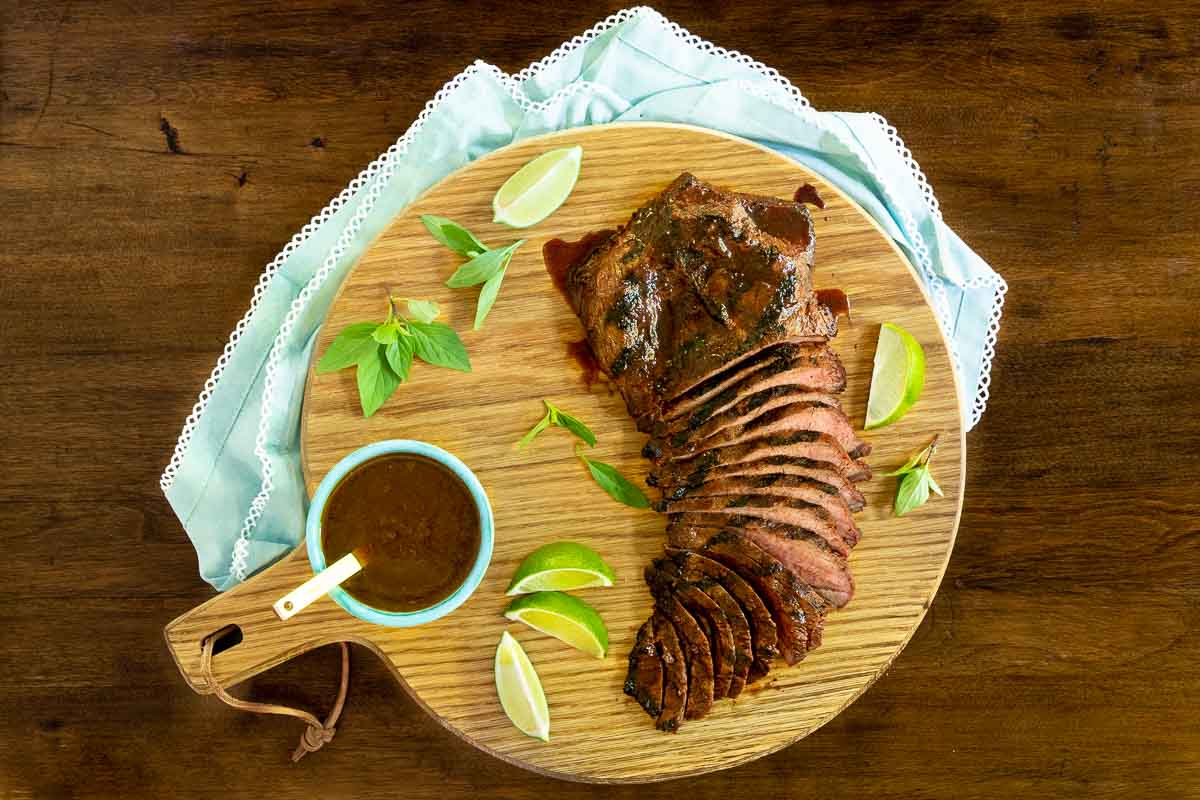 Horizontal overhead photo of Steve's Grilled Asian Steak sliced on a round wood cutting board.