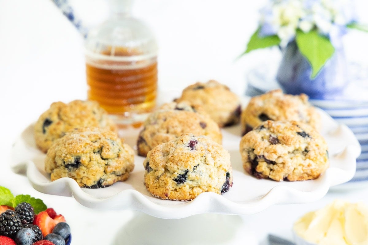 Horizontal photo of a batch of Lemon Blueberry Scones on a scalloped pedestal serving plate.