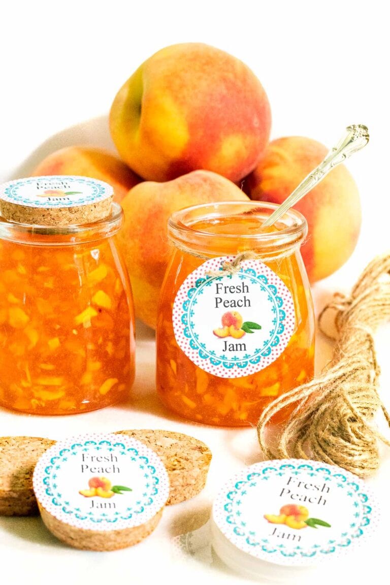 Peach jam in glass jars with labels and fresh peaches in the background