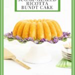 Vertical photo of a Sugar-Glazed Ricotta Bundt Cake on a white scalloped pedestal plate decorated with fresh rosemary and lavender sprigs.