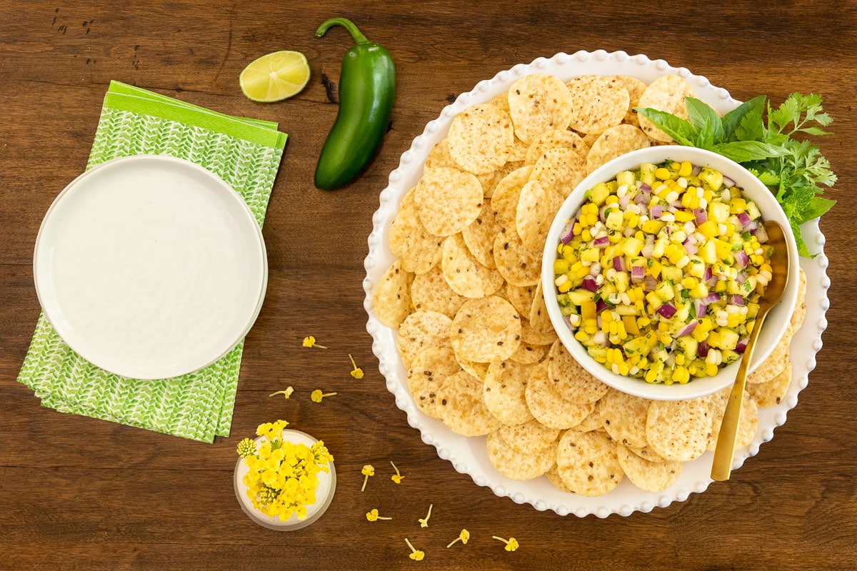 Horizontal overhead photo of Asian Pineapple Fresh Corn Salsa surrounded by tortilla chips on a wood table.