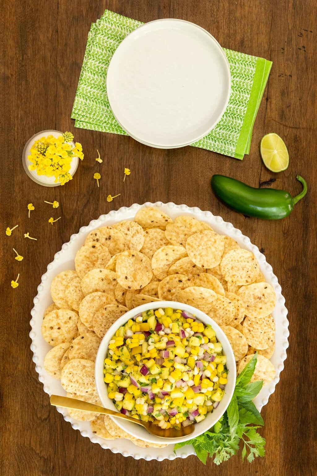 Vertical overhead photo of a bowl of Asian Pineapple Fresh Corn Salsa surrounded by tortilla chips on a wood table.
