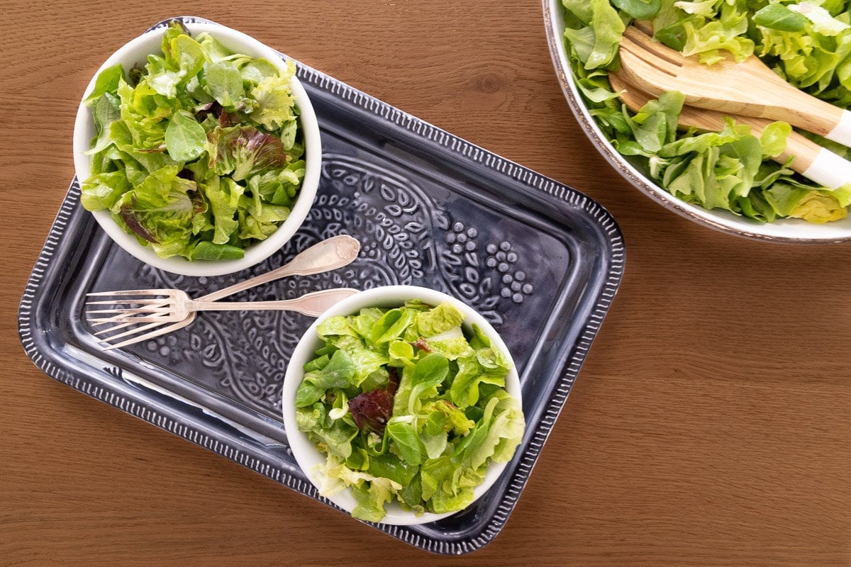 Horizontal overhead photo of two serving bowls of Classic French Bistro Salad on a wood table.
