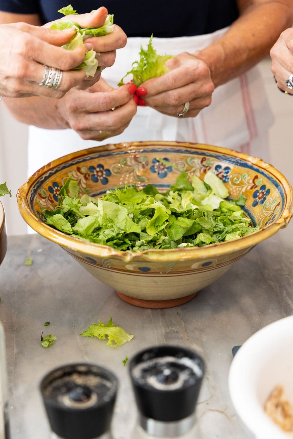 Vertical closeup photo of several people breaking up lettuce for a French Bistro Salad.