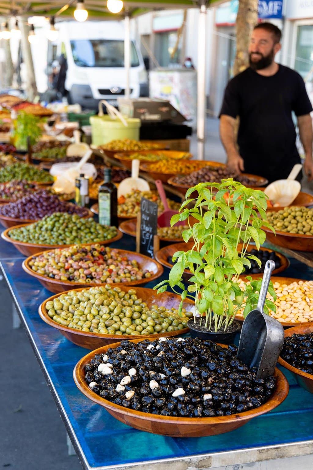 Vertical photo of long tables of a wide variety of olives at the French market in Lyon, France.