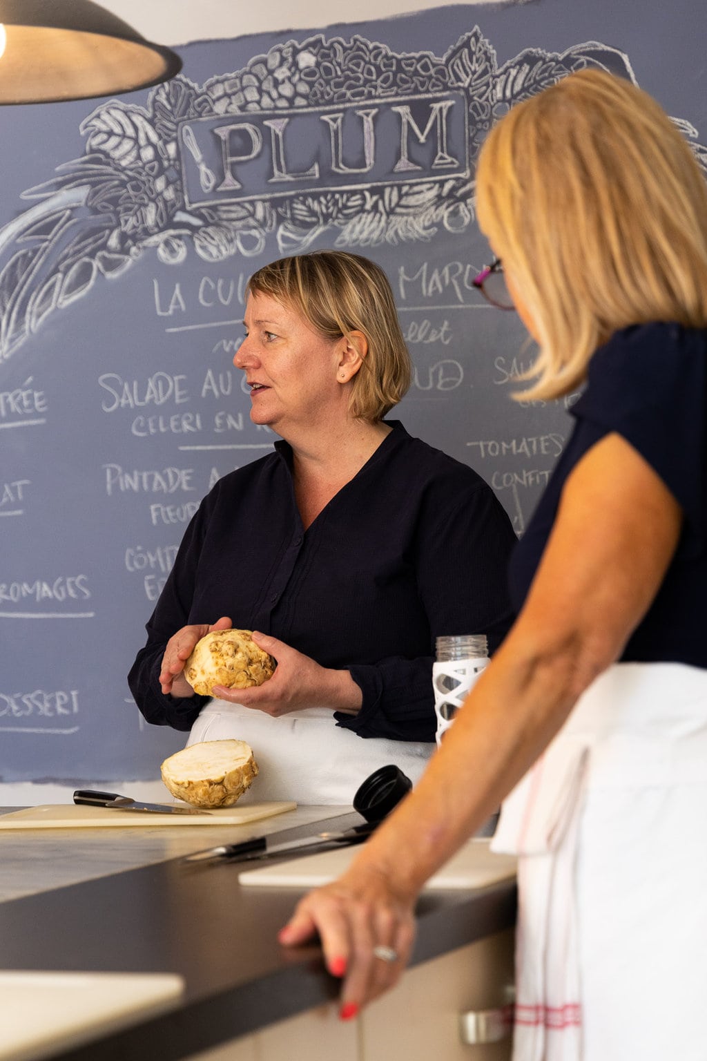 Vertical photo of Lucy teaching her students at Plum Cooking school in Lyon, France.