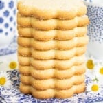 Horizontal closeup photo of a stack of French Shortbread Cookies (Sablés Bretons) surrounded by flowers and cups of milk.