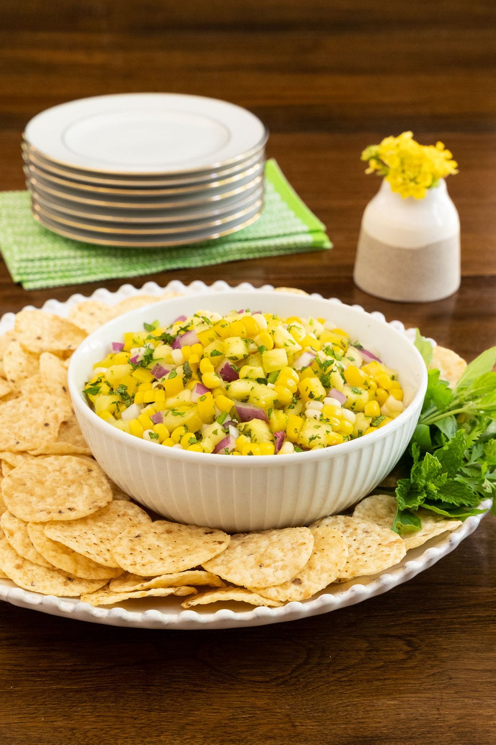 Vertical photo of a bowl of Asian Pineapple Fresh Corn Salsa on a serving plate filled with tortilla chips.