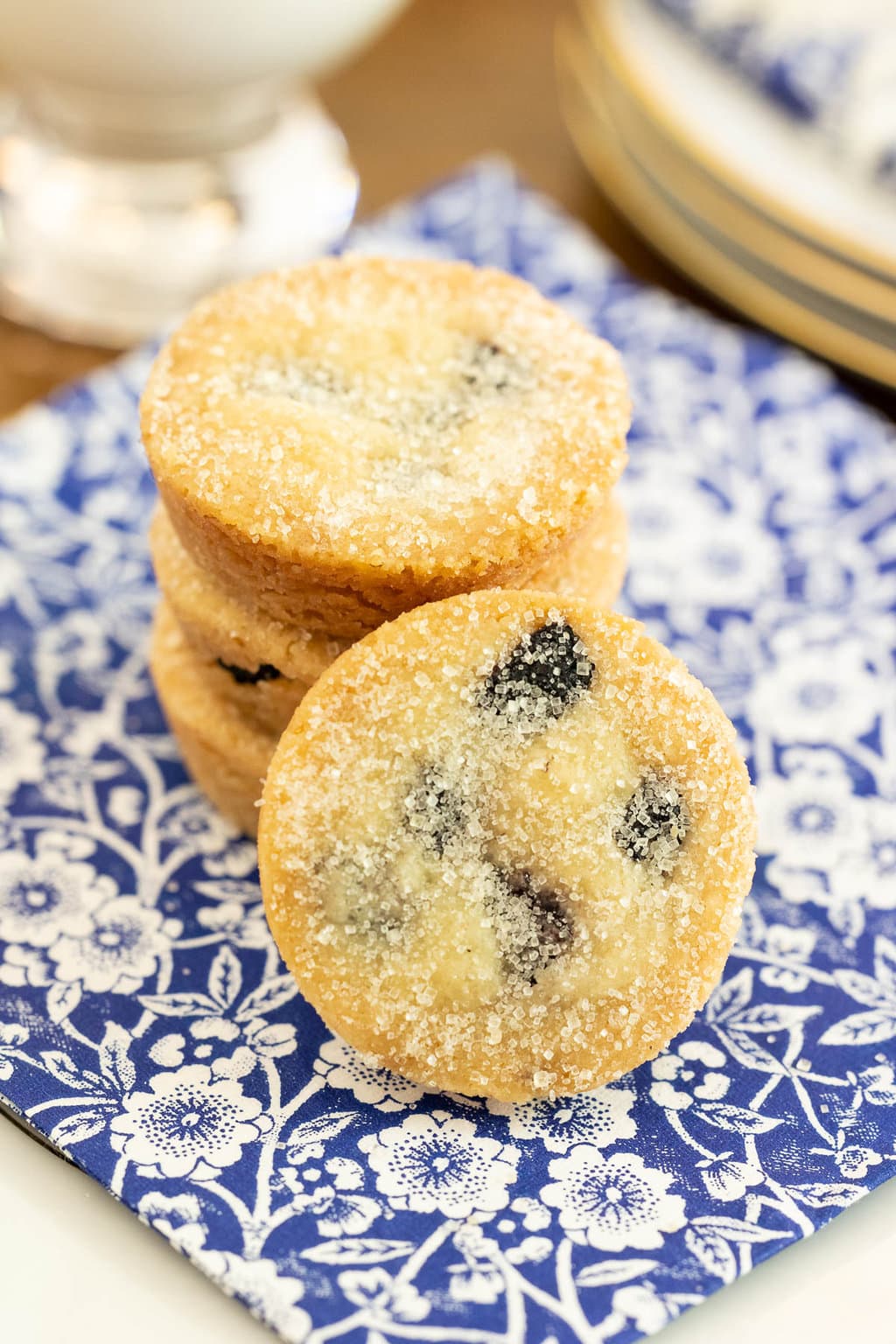 Vertical closeup photo of a stack of Ridiculously Easy Lemon Blueberry Shortbread Bites on a blue and white patterned napkin.