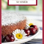 Vertical closeup photo of a Ridiculously Fresh Sweet Cherry Almond Cake on a white pedestal cake stand surrounded by fresh cherries and daisies with a title graphic at the top of the photo.
