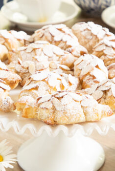 Horizontal closeup photo of a batch of Ridiculously Easy Almond Croissants on a white scalloped serving pedestal plate.