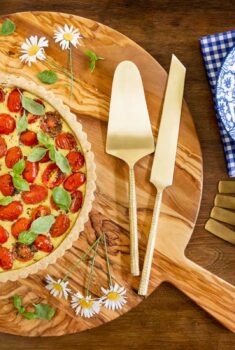 Horizontal overhead photo of a French Tomato Ricotta Tart on a round wood cutting board.